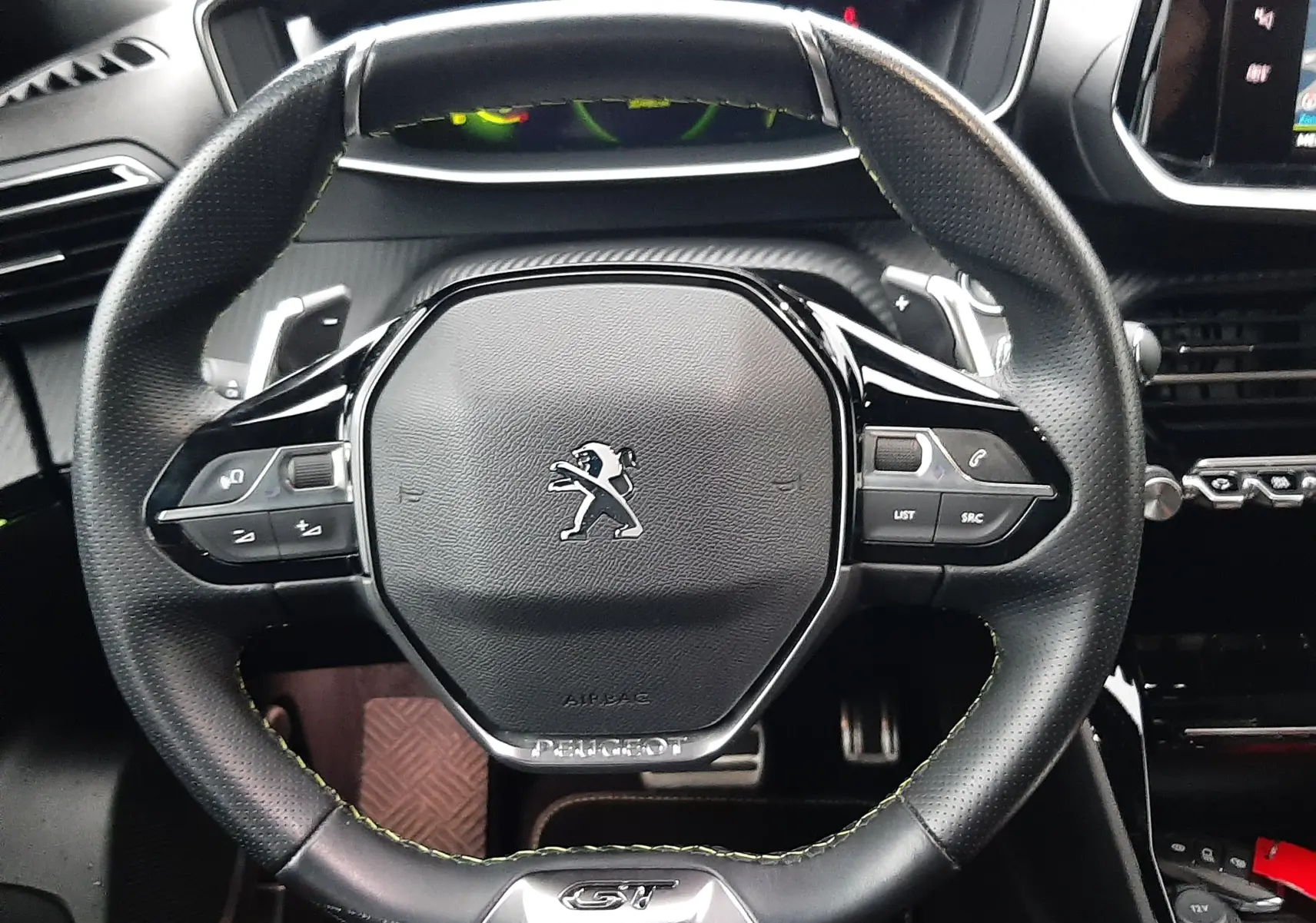 Vue rapprochée du volant cuir GT du Peugeot 2008 2023 avec commandes intégrées et tableau de bord en arrière-plan.