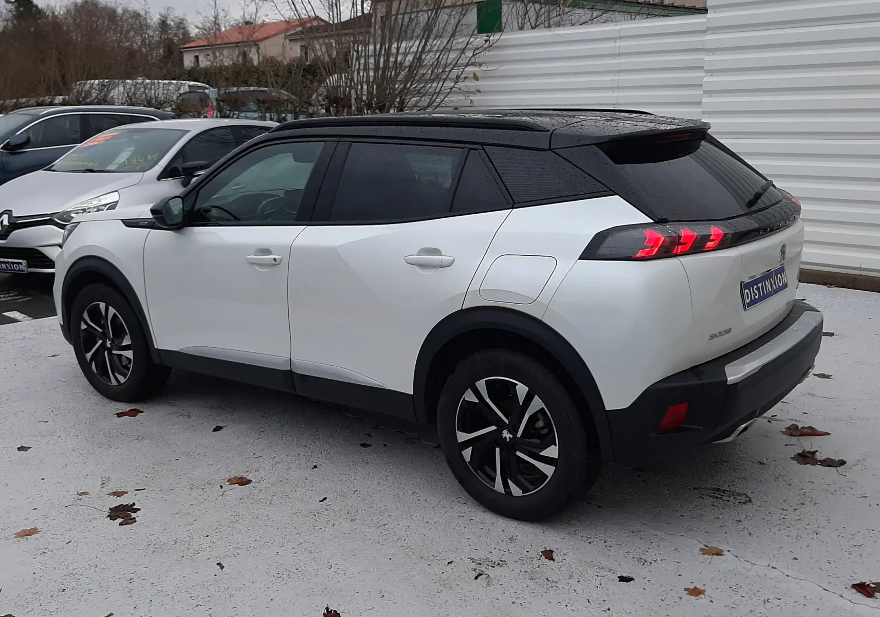 Peugeot 2008 blanc nacré avec toit noir en vue 3/4 arrière droit, feux arrière allumés et attelage visible.