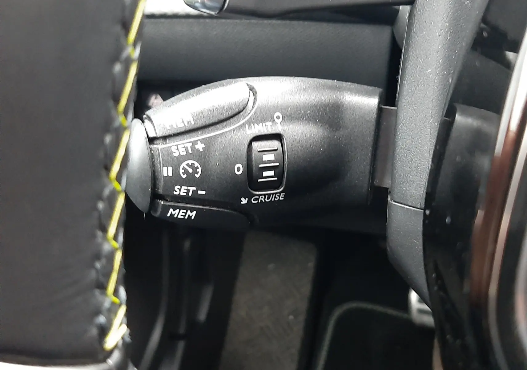 Gros plan sur la commande de régulateur de vitesse au volant cuir noir avec surpiqûres jaunes d'une Peugeot 2008 blanche nacrée 2023.