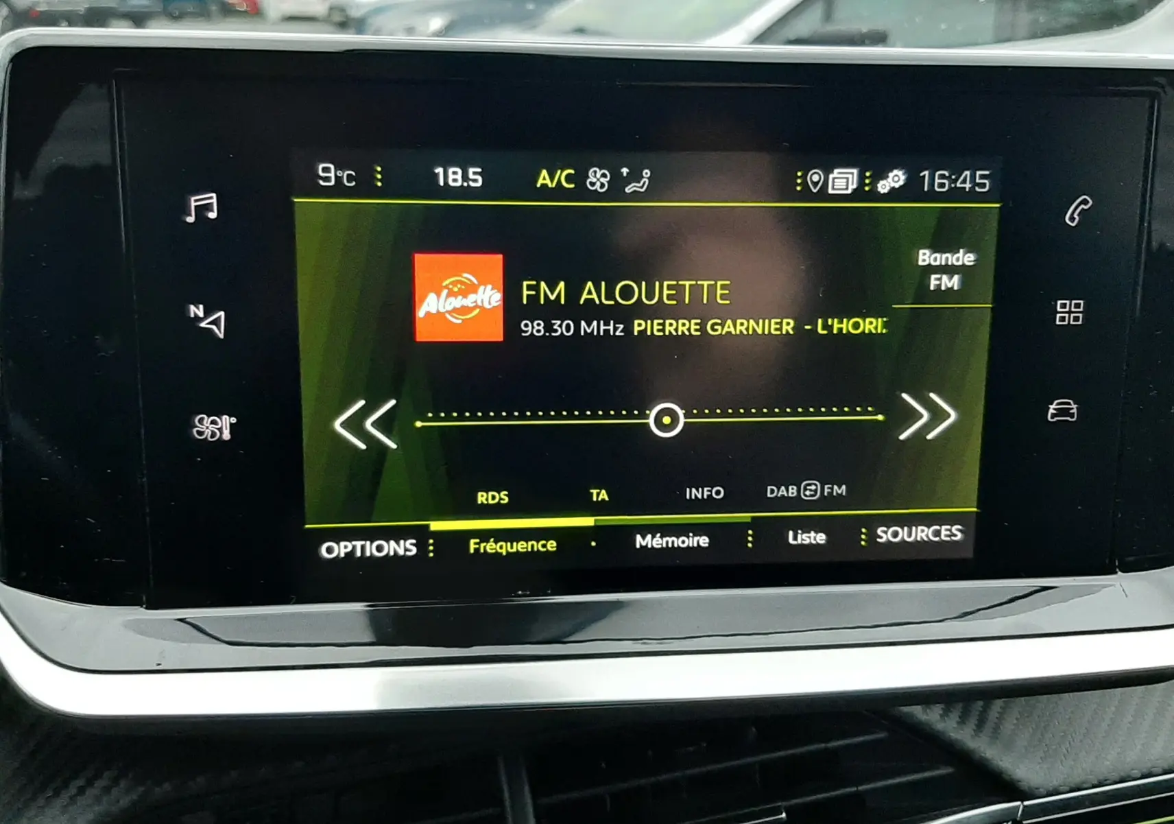 Écran tactile central du Peugeot 2008 2023 affichant la radio FM Alouette, avec tableau de bord noir et extérieur flou.