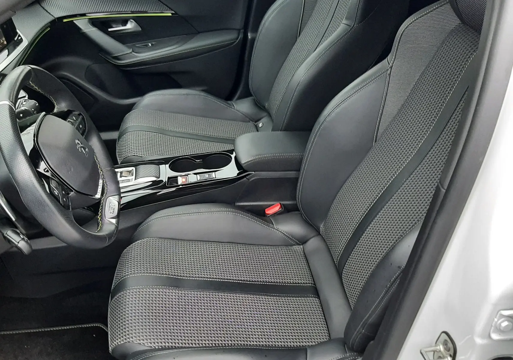 Vue intérieure côté conducteur du Peugeot 2008 2023 blanc nacré, sièges noirs en cuir et tissu avec console centrale brillante.