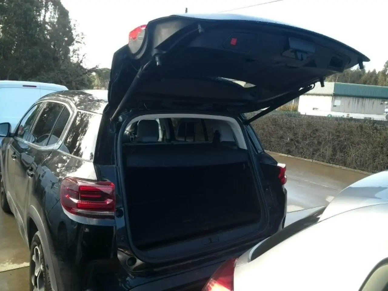 Vue arrière 3/4 gauche du Citroën C5 Aircross noir Perla avec hayon électrique ouvert montrant le coffre vide.