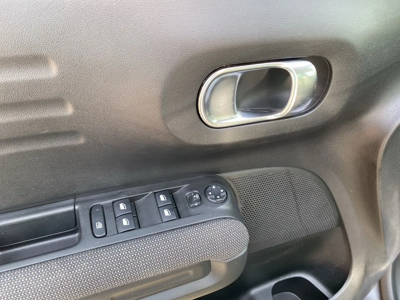 Gros plan sur la porte côté conducteur de la Citroën C3 Aircross gris platinium, montrant les commandes des vitres et la poignée intérieure.