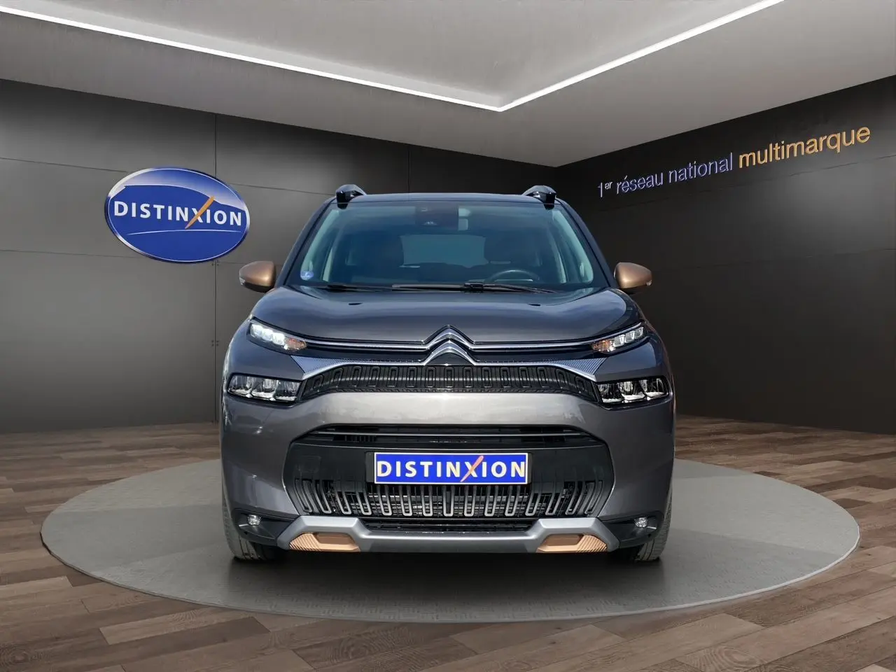 Vue frontale d'un Citroën C3 Aircross gris platinium avec détails bronze sur les rétroviseurs et pare-chocs, en showroom.