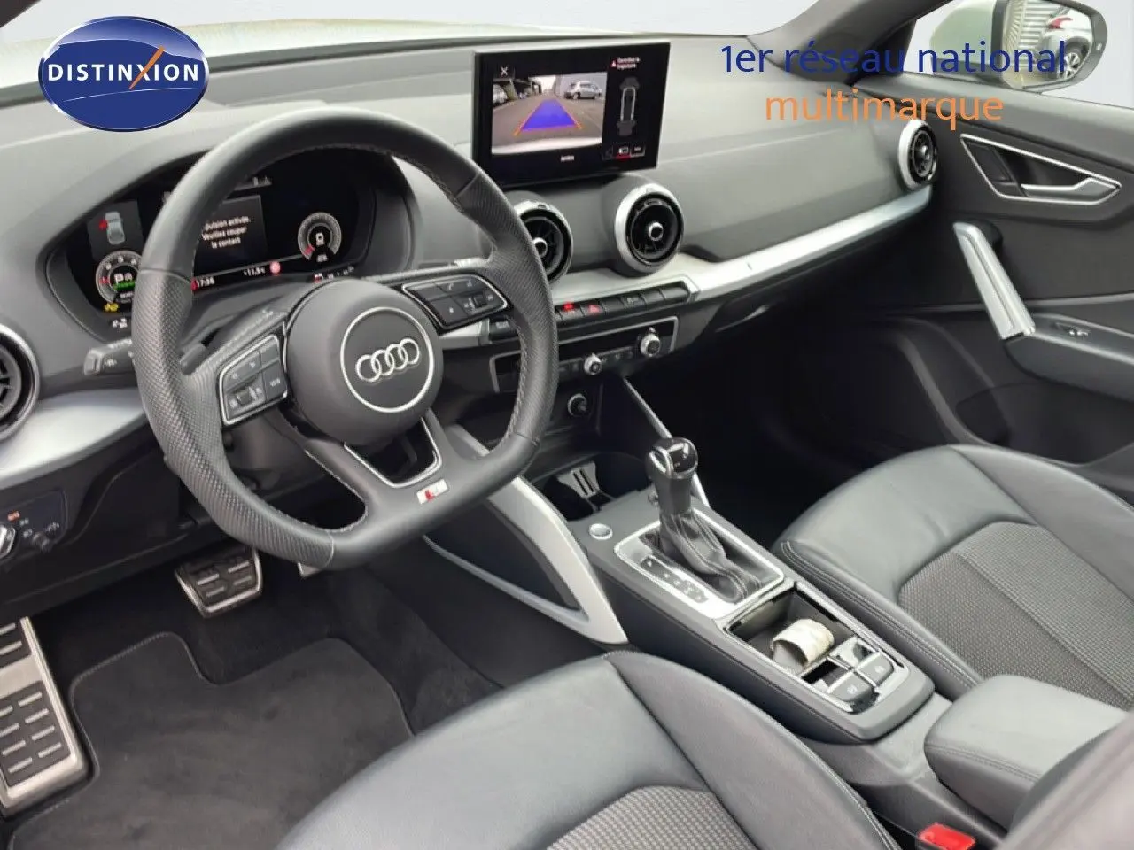 Vue intérieure côté conducteur de l'Audi Q2 35 2.0 TDI S-Line 2025 avec volant cuir perforé et écran multimédia central.
