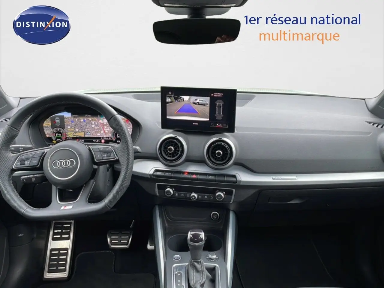 Intérieur Audi Q2 2025 vu de face, tableau de bord noir avec écran central affichant caméra de recul.