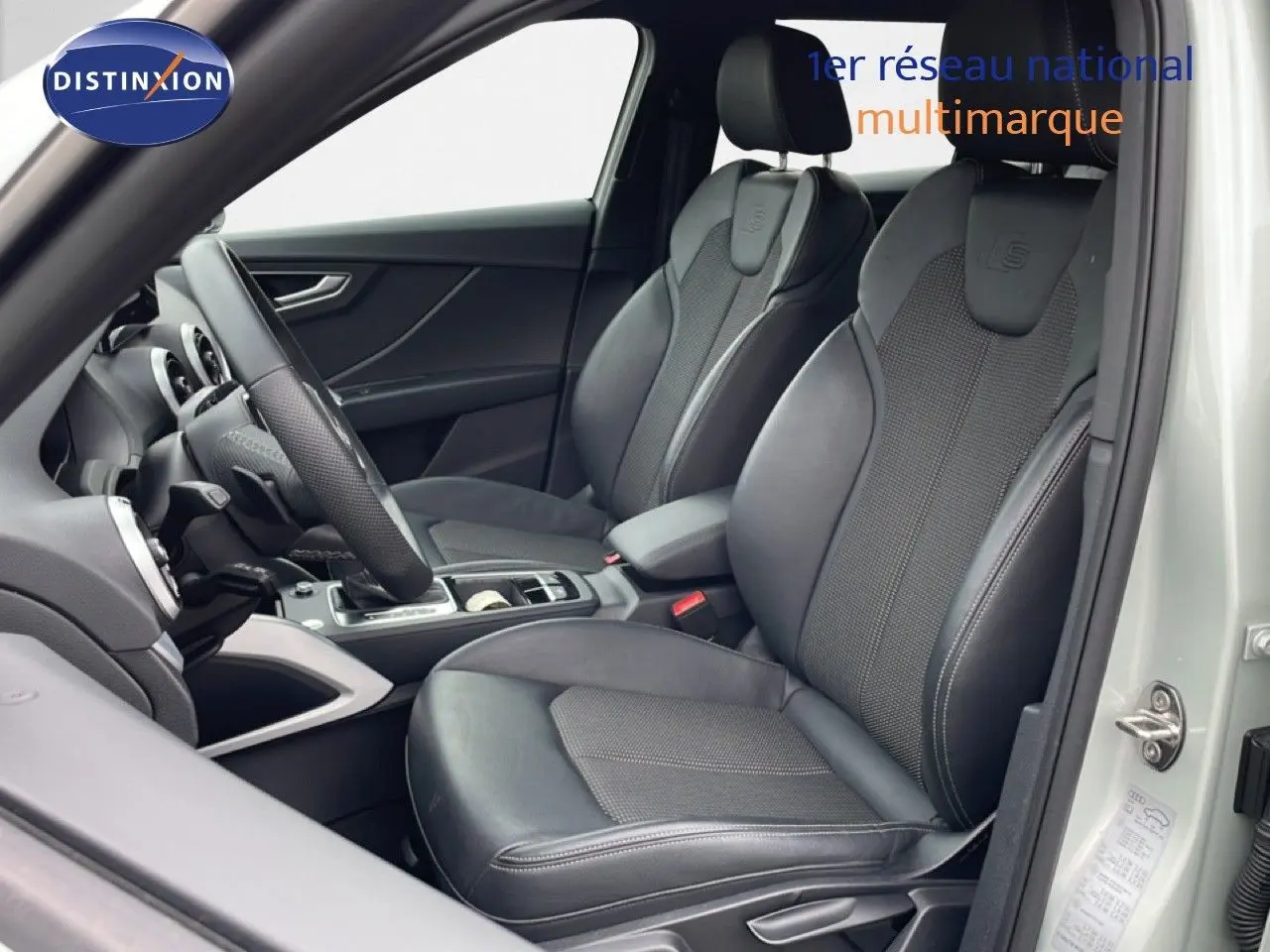 Vue intérieure côté conducteur de l'Audi Q2 argent rose métal, sièges sport cuir noir avec logo S-Line embossé.
