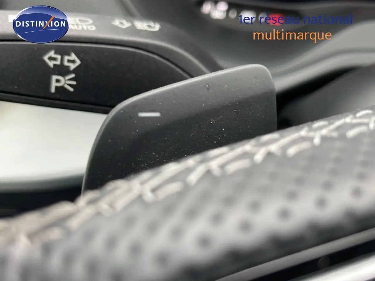 Gros plan sur la palette de changement de vitesse derrière le volant perforé de l'Audi Q2 argent rose métal.