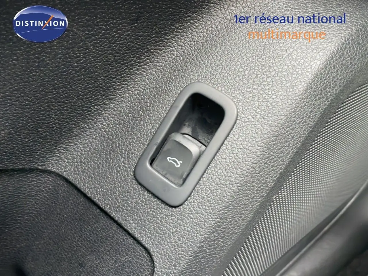 Gros plan sur le bouton d'ouverture du coffre intégré dans le revêtement noir texturé de l'Audi Q2.