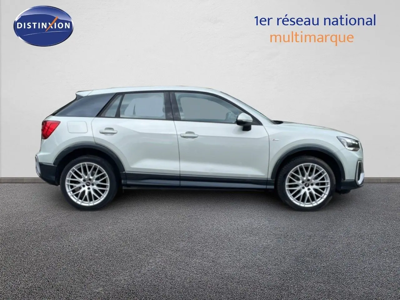 Audi Q2 argent rose métal en profil droit, avec jantes alliage et toit noir contrasté, sur fond neutre.