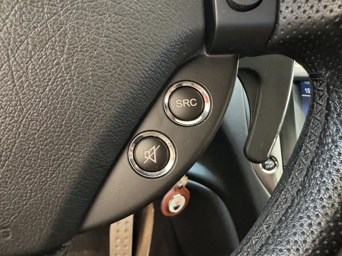 Gros plan sur les commandes audio au volant en cuir noir perforé de la Maserati Granturismo S 4.7 gris foncé de 2010.