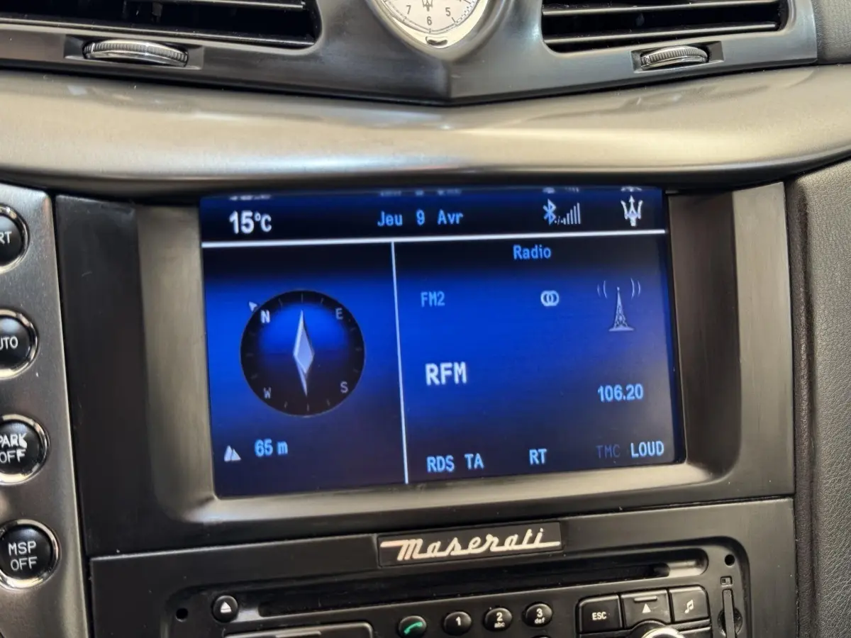Gros plan sur l’écran central bleu du système multimédia de la Maserati Granturismo S 4.7, avec horloge et logo Maserati.