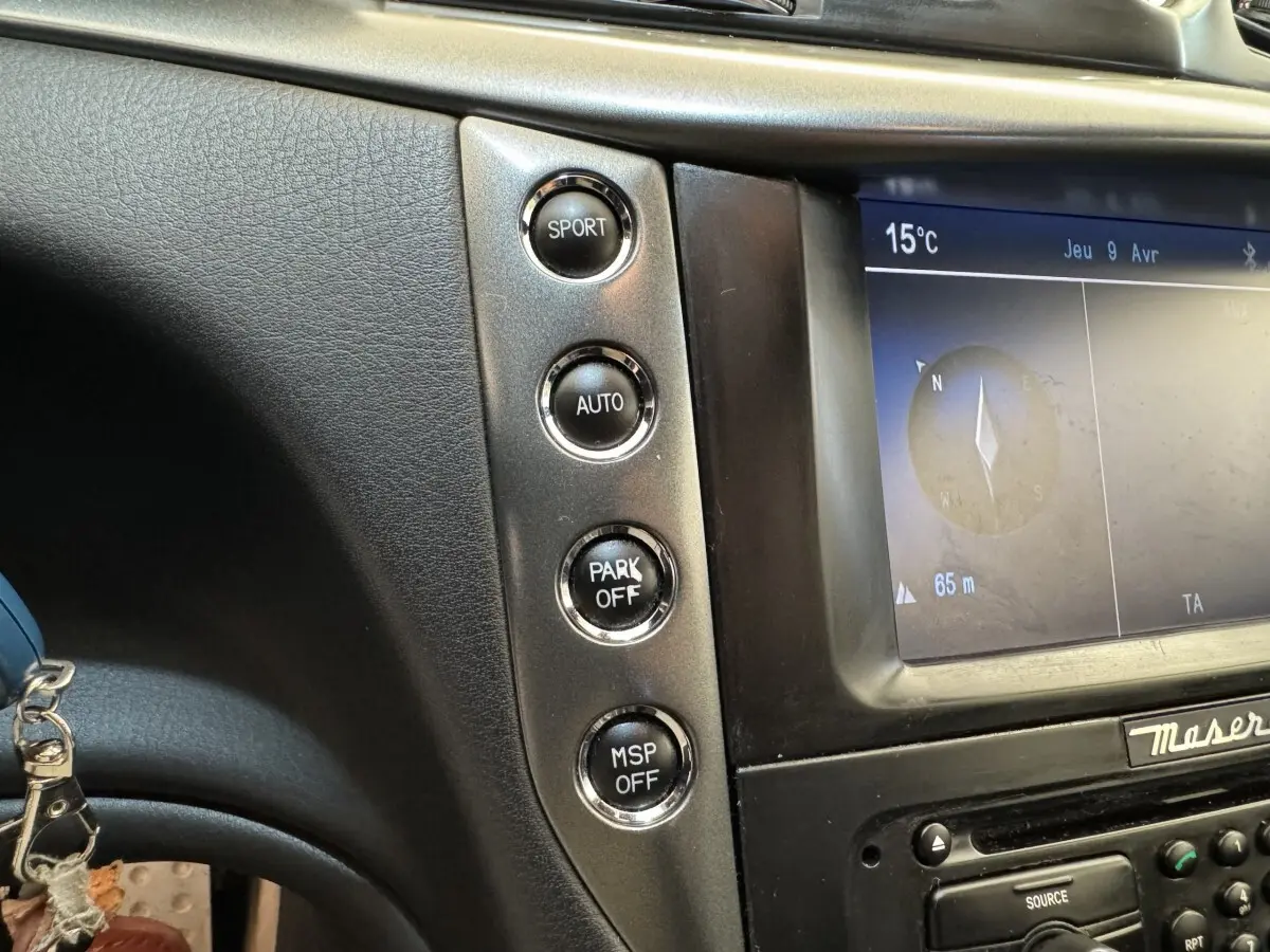 Gros plan sur la console centrale de la Maserati Granturismo S 4.7 2010, boutons de mode sport et écran de navigation visible.