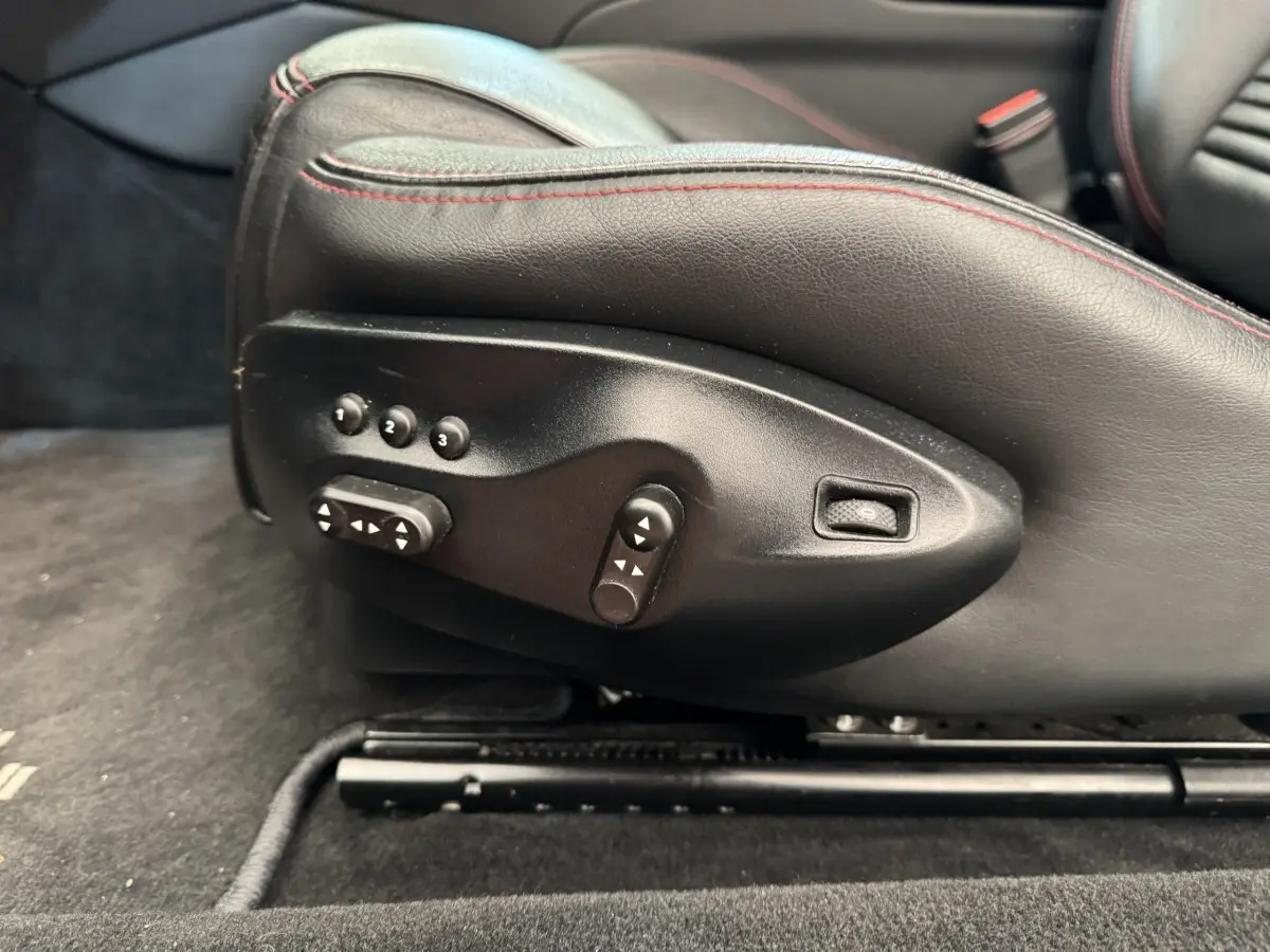 Gros plan sur les commandes électriques du siège conducteur en cuir noir avec surpiqûres rouges d'une Maserati Granturismo S 4.7 gris foncé.