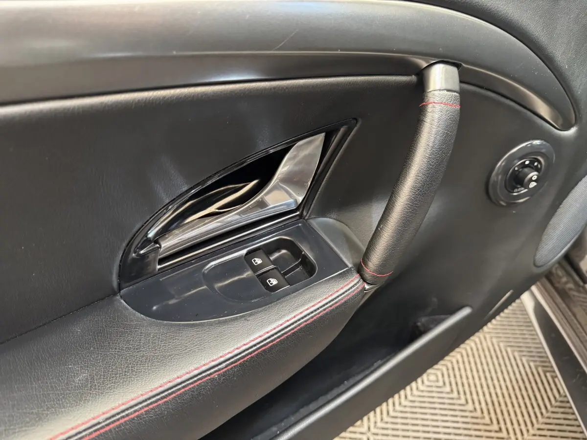 Gros plan sur la poignée et les commandes de fenêtre côté gauche de la porte intérieure noire avec surpiqûres rouges d'une Maserati Granturismo S 4.7.