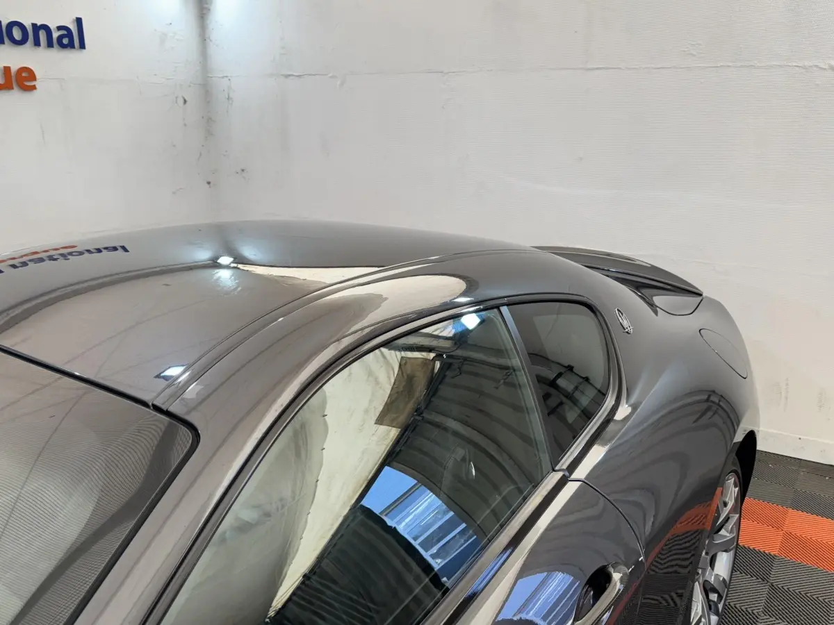 Vue 3/4 arrière droite d'une Maserati Granturismo S 4.7 gris foncé avec spoiler de coffre et jantes argentées.
