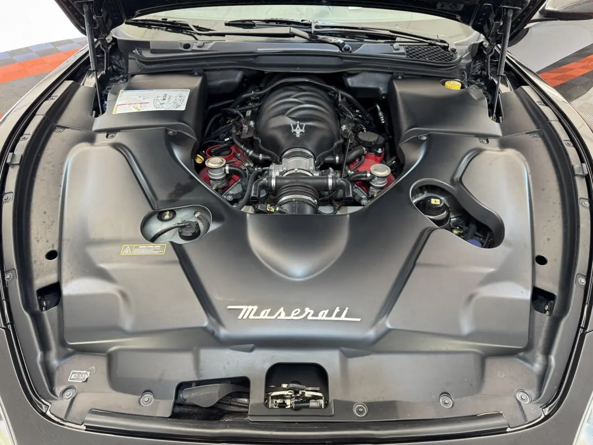 Vue plongeante sur le moteur noir de la Maserati Granturismo S 4.7 gris foncé avec logo Maserati visible.