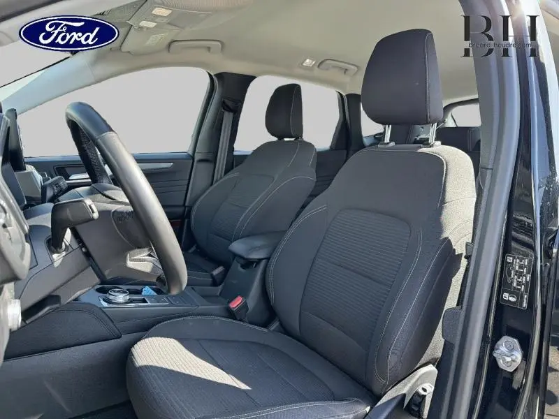Vue intérieure côté conducteur de la Ford Kuga 2023 noir Agate, sièges sport noirs et volant cuir multifonction.