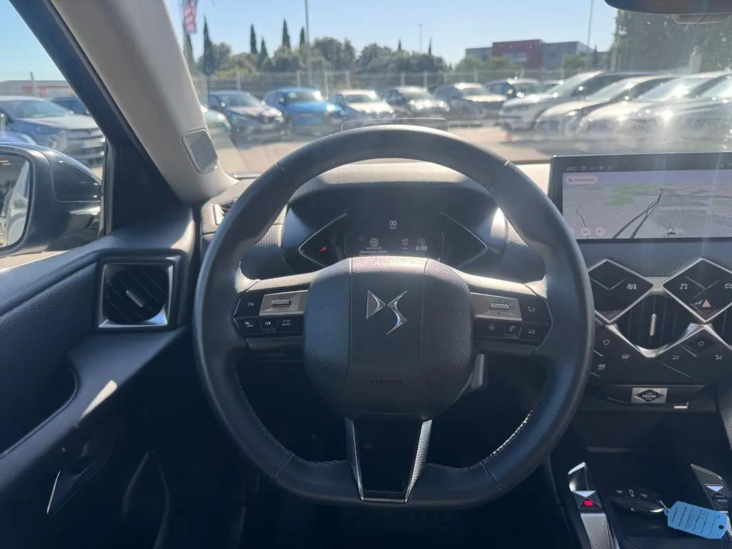 Vue intérieure centrée sur le volant DS d’une DS3 2024, avec tableau de bord numérique et écran tactile de navigation.