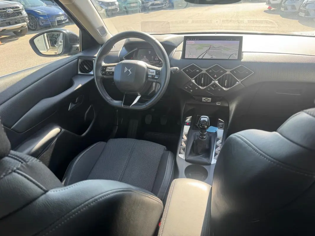 Vue intérieure avant du DS3 2024 gris, montrant le volant, la boîte manuelle et l'écran tactile central avec navigation.