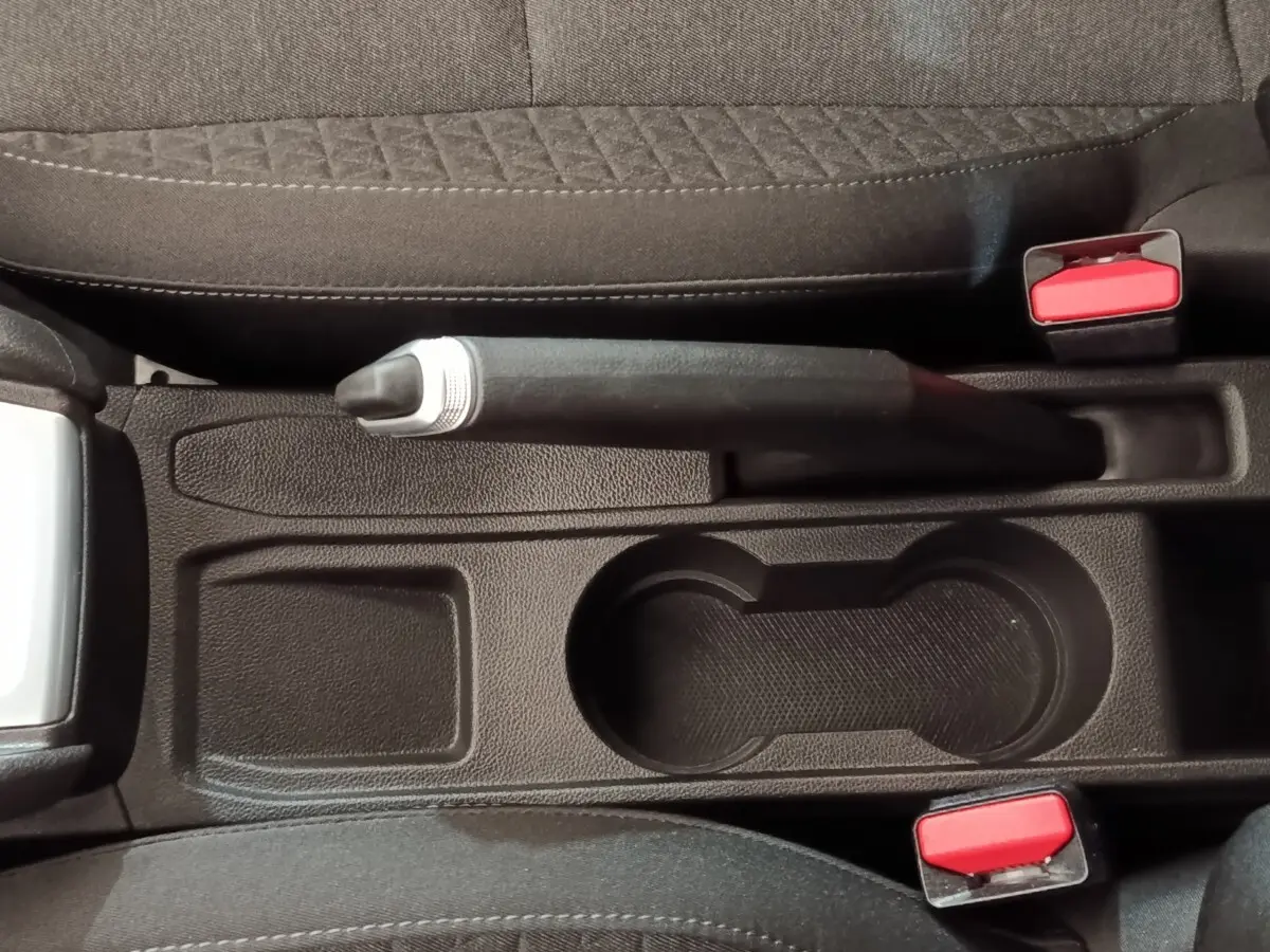 Vue plongeante sur la console centrale noire de la Renault Clio Business E-TECH 140 avec frein à main manuel et porte-gobelets.