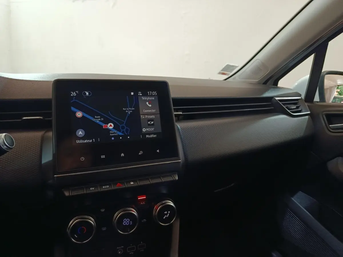 Vue intérieure du tableau de bord de la Renault Clio Business E-TECH 140 blanc, avec écran tactile de navigation allumé.