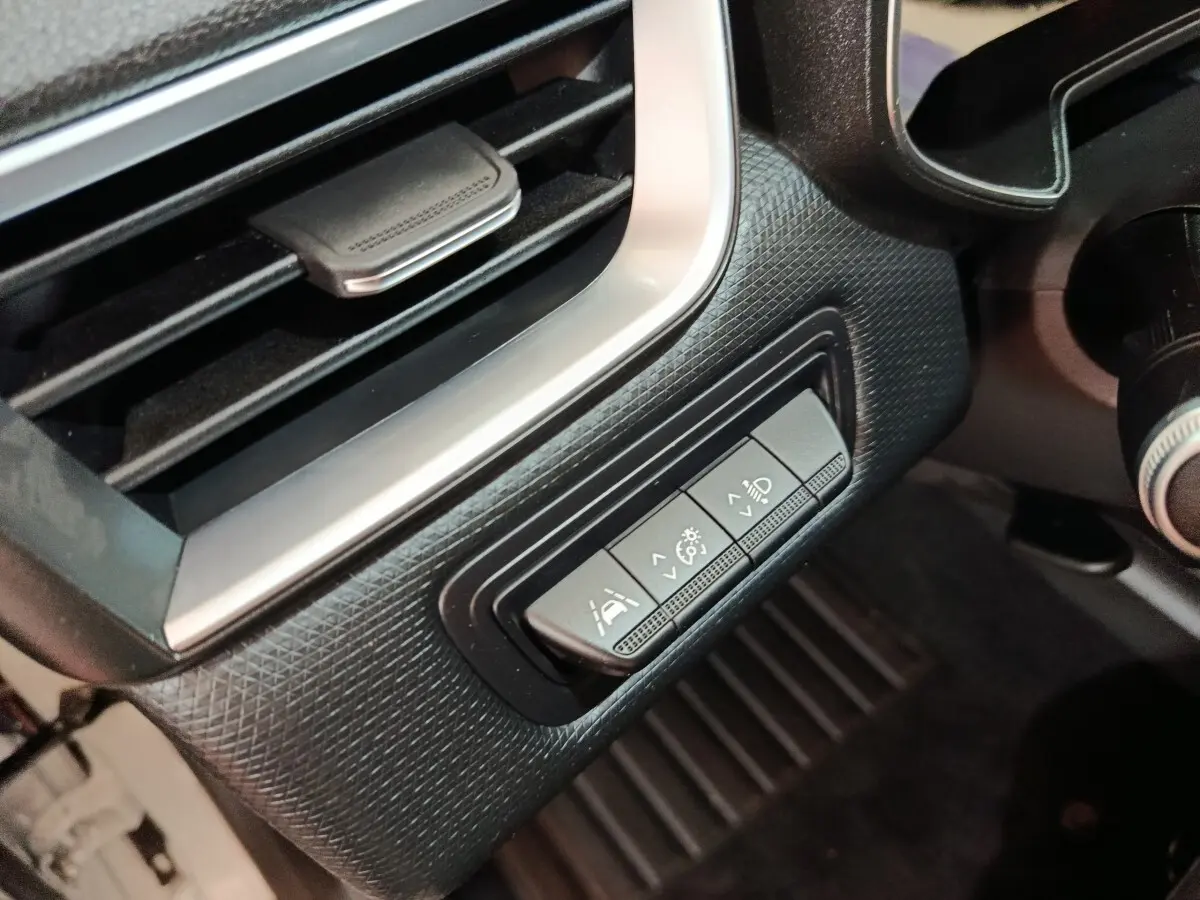 Gros plan sur les commandes d'assistance à la conduite et réglage des phares dans l'habitacle de la Renault Clio Business E-TECH 140 blanche.