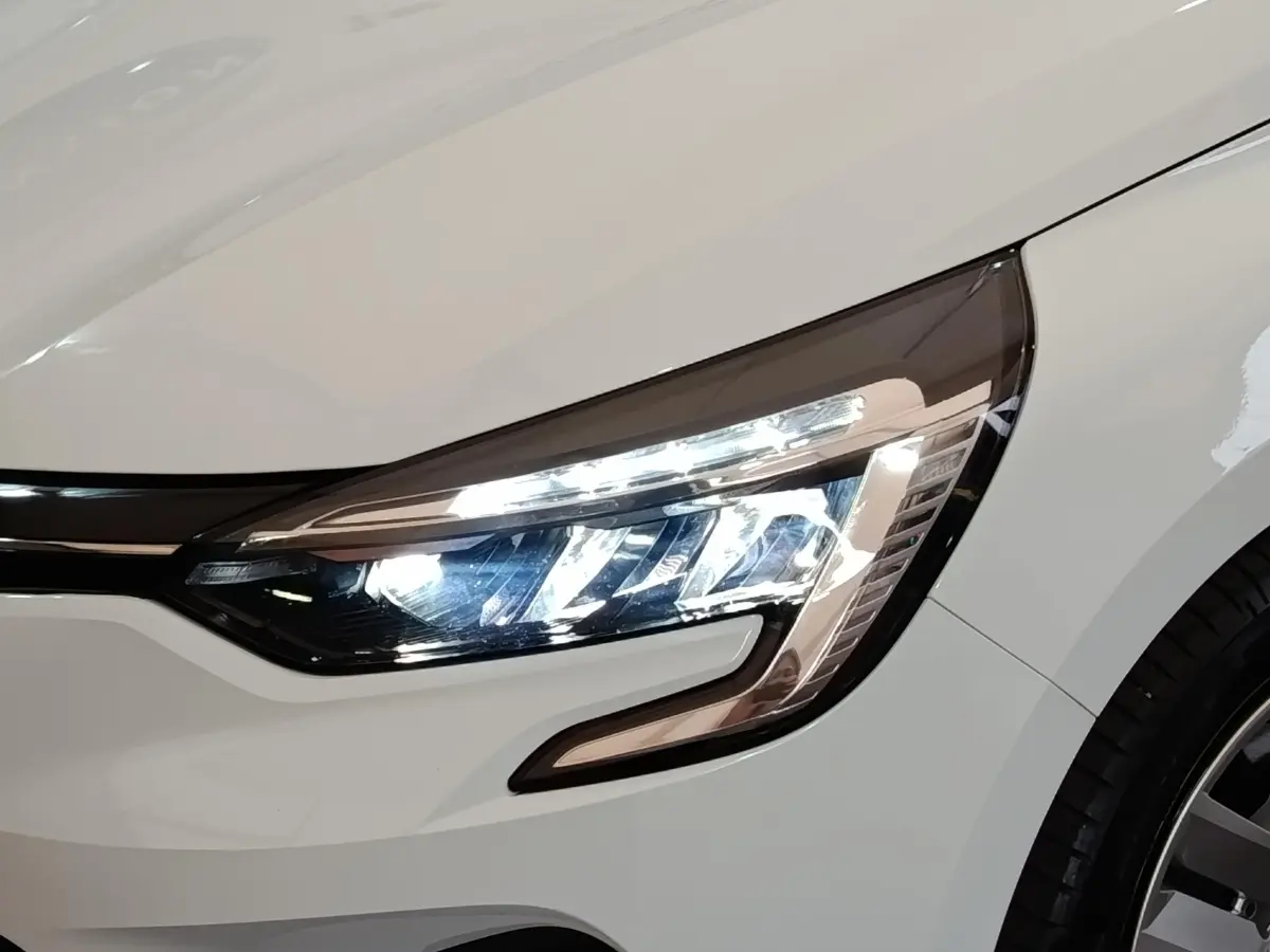 Gros plan sur le phare avant droit allumé d'une Renault Clio Business E-TECH blanche de 2021.
