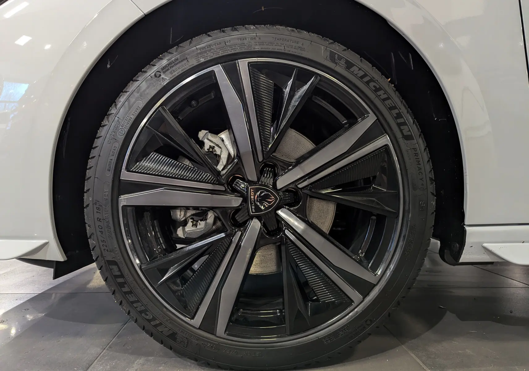 Gros plan sur la roue avant droite d'une Peugeot 308 GT blanche, avec jante alliage noire et grise au design moderne.