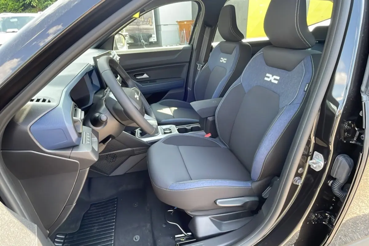 Intérieur du Dacia Bigster TCE 130 4x4 Expression Plus 2025, sièges avant noirs et bleus avec logo DC visibles côté conducteur.