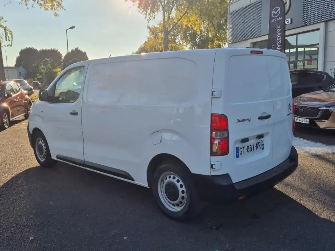 Vue 3/4 arrière droite d'un Citroën Jumpy blanc fourgon L2H1 avec hayon, stationné en extérieur au soleil.