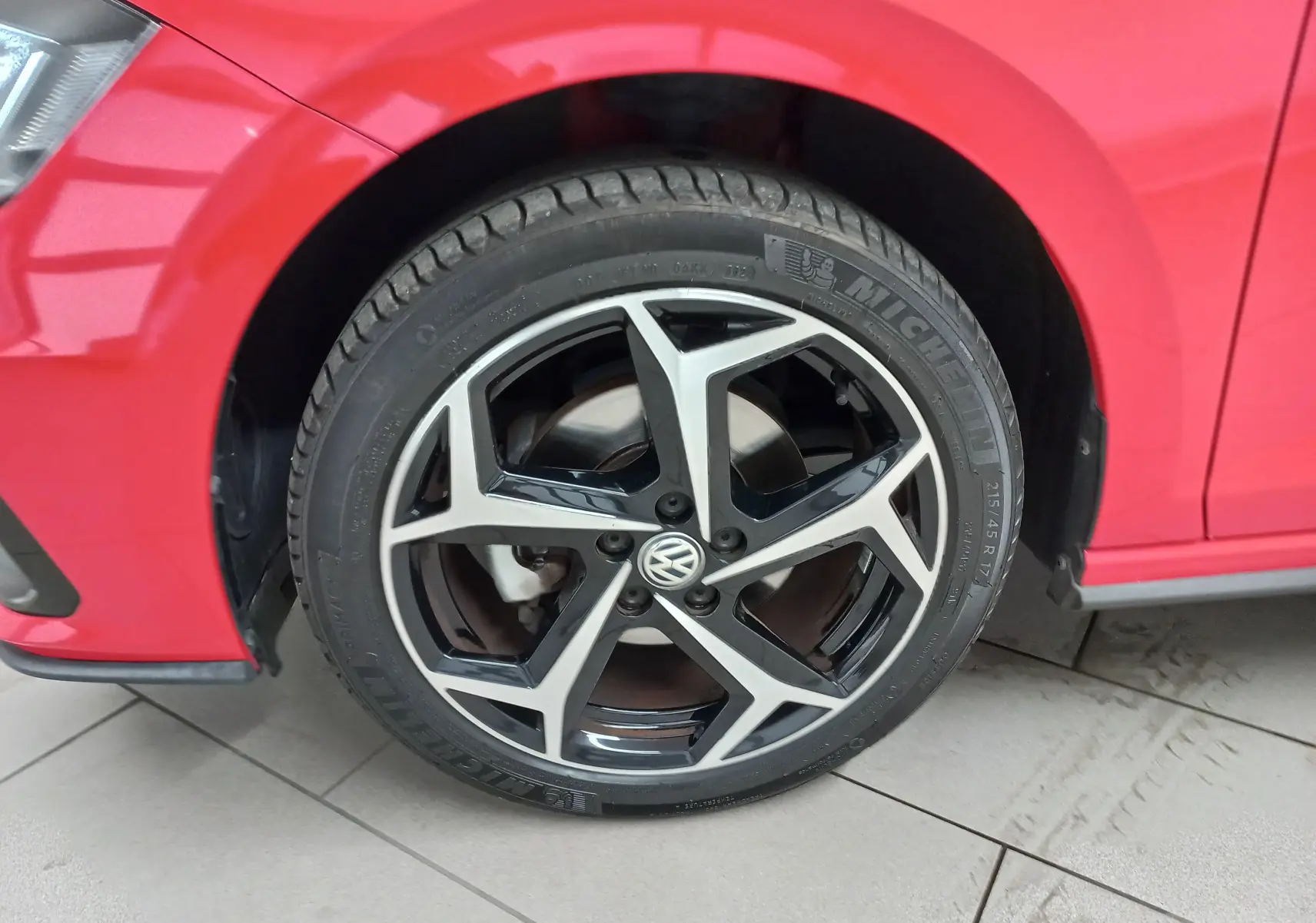 Gros plan sur la roue avant gauche d'une Volkswagen Polo Rouge Flash avec jante alliage R-Line bicolore.