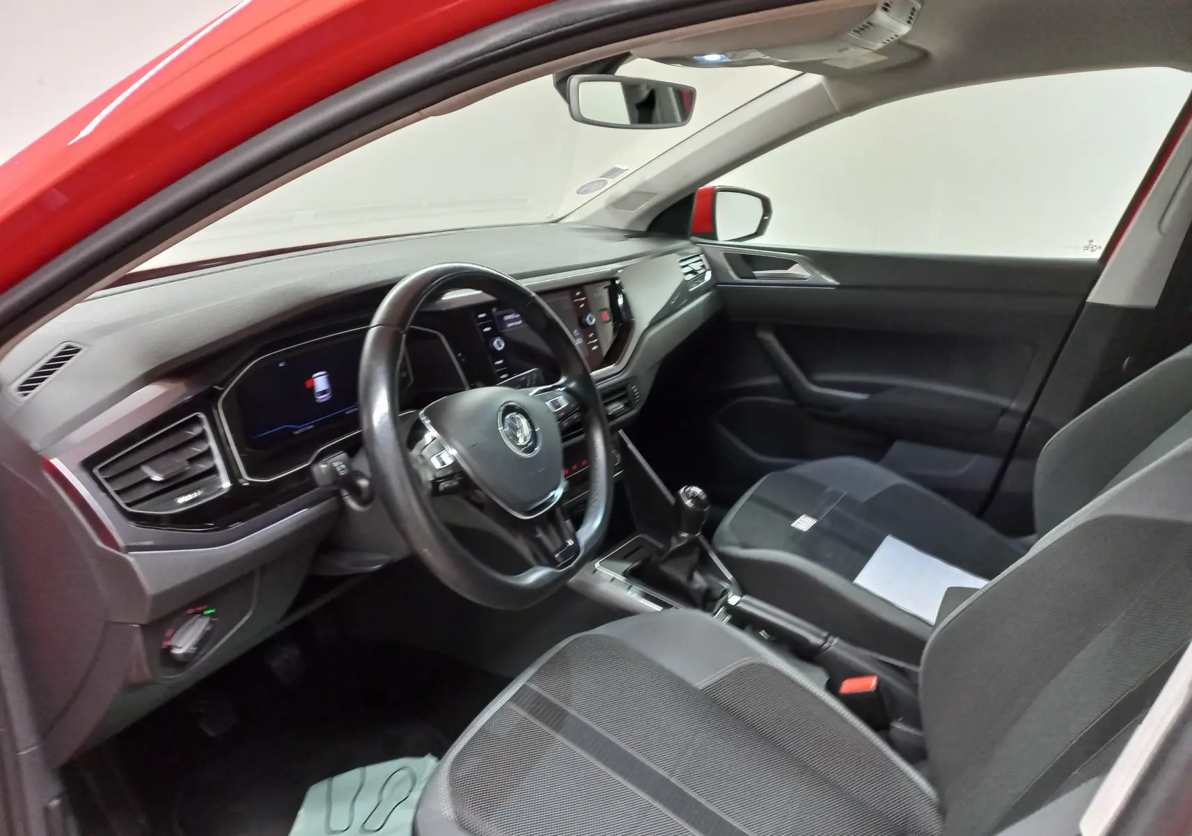 Vue intérieure côté conducteur d'une Volkswagen Polo Rouge Flash 2019 avec tableau de bord numérique et boîte manuelle.