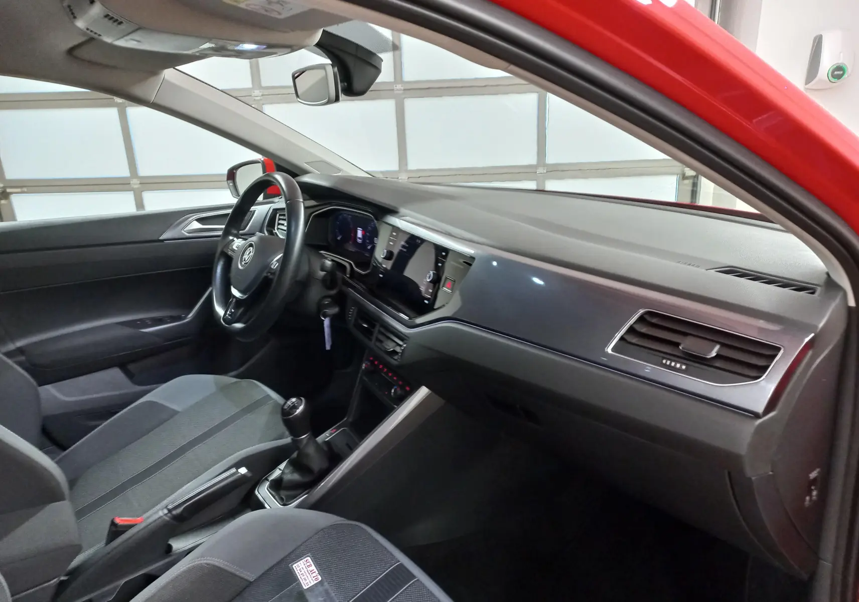 Intérieur côté conducteur d'une Volkswagen Polo Rouge Flash 2019, tableau de bord moderne avec écran digital et boîte manuelle.