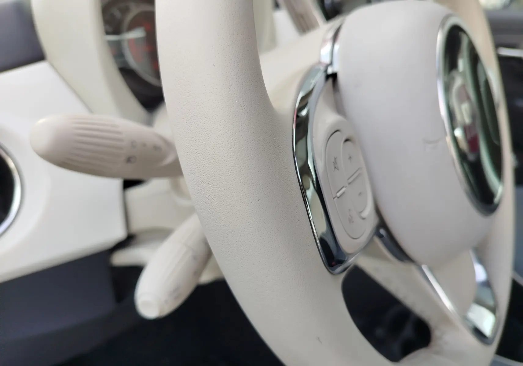 Gros plan sur le volant blanc Bossa Nova de la Fiat 500 Lounge 2017 avec commandes intégrées et détails chromés.