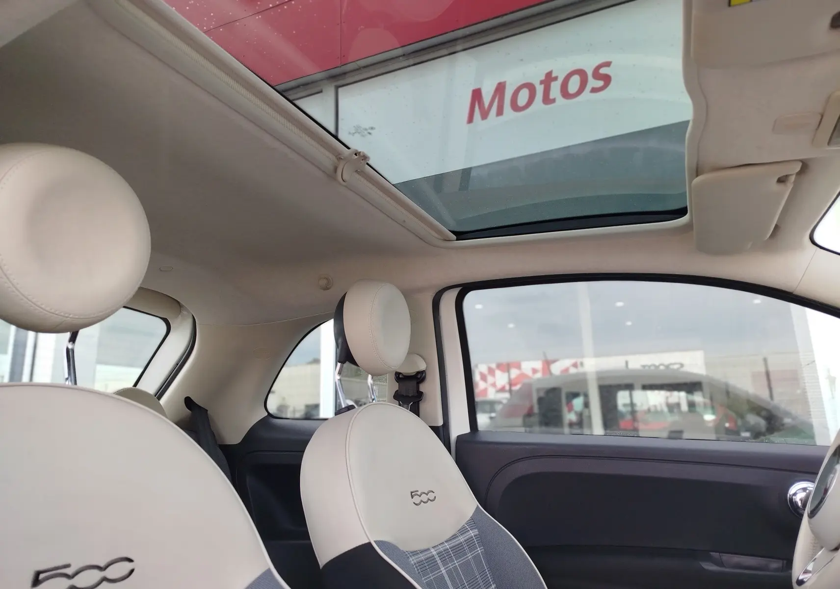 Vue intérieure côté droit de la Fiat 500 Lounge blanche, avec toit ouvrant et sièges avant en cuir clair brodés 500.