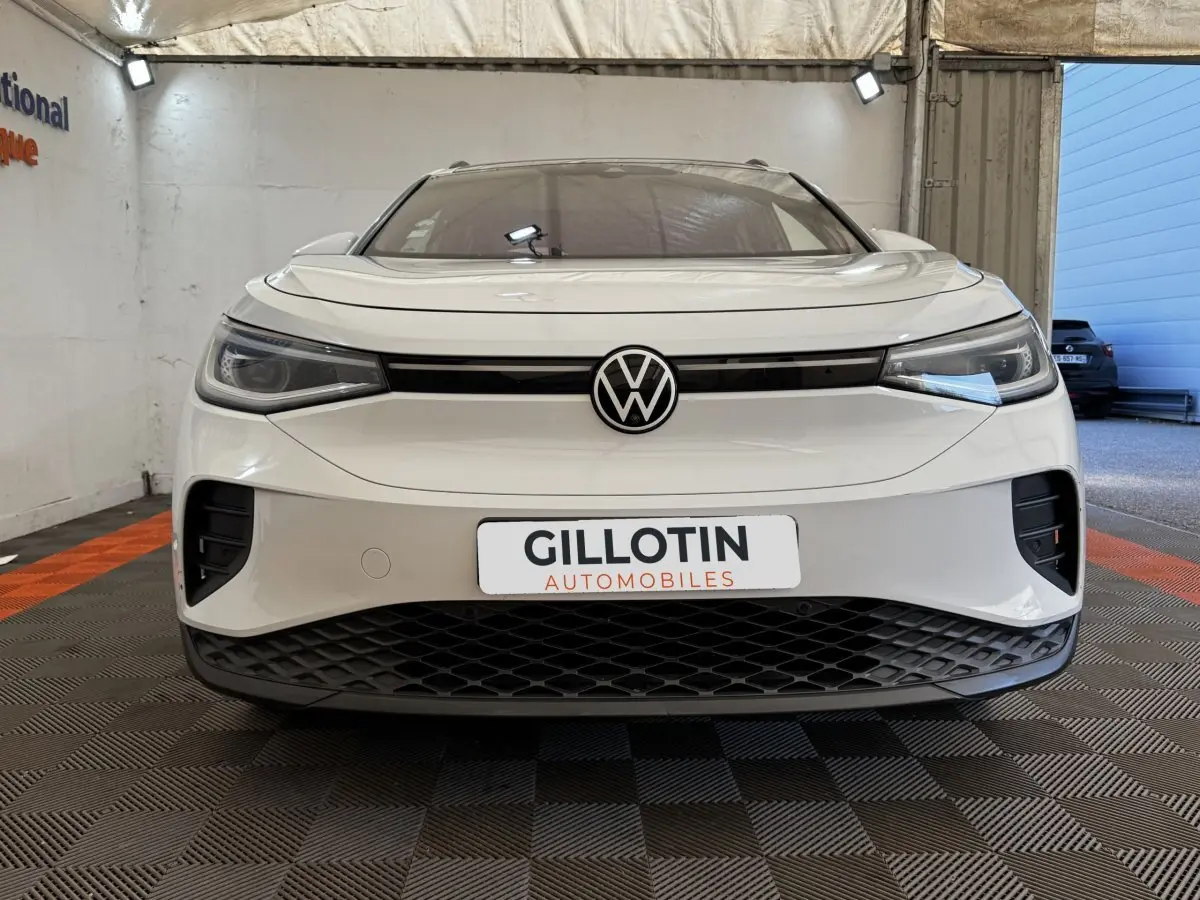 Vue frontale d’un Volkswagen ID.4 blanc avec calandre noire et logo VW centré, en intérieur showroom.