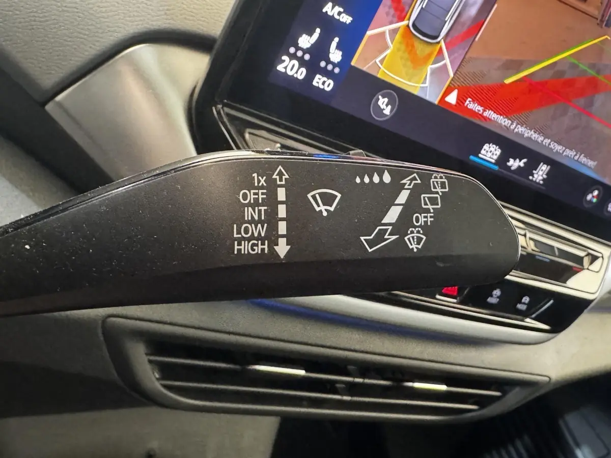 Gros plan sur la commande d’essuie-glace à gauche dans l’habitacle du Volkswagen ID.4 blanc, avec écran tactile en arrière-plan.