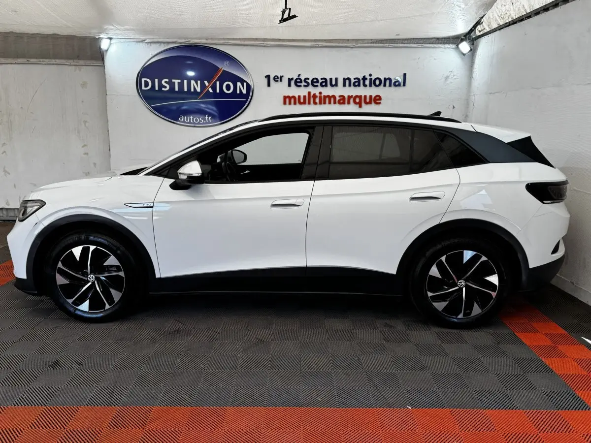 Vue de profil côté gauche d'un Volkswagen ID.4 blanc avec jantes noires et toit noir dans un showroom.