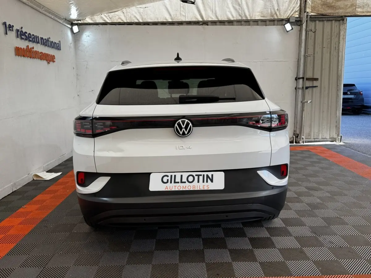 Vue arrière d’un Volkswagen ID.4 blanc avec feux arrière en bandeau et logo VW centré, stationné en intérieur.