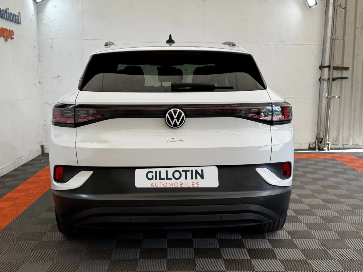 Vue arrière d'un Volkswagen ID.4 blanc avec feux arrière LED reliés et logo VW centré dans un garage.