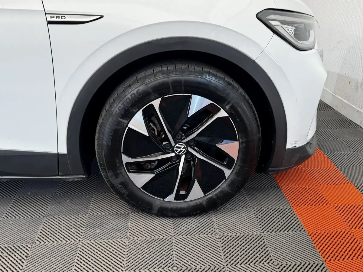 Gros plan sur la roue avant droite d’un Volkswagen ID.4 blanc avec jante noire et argentée, badge Pro visible.