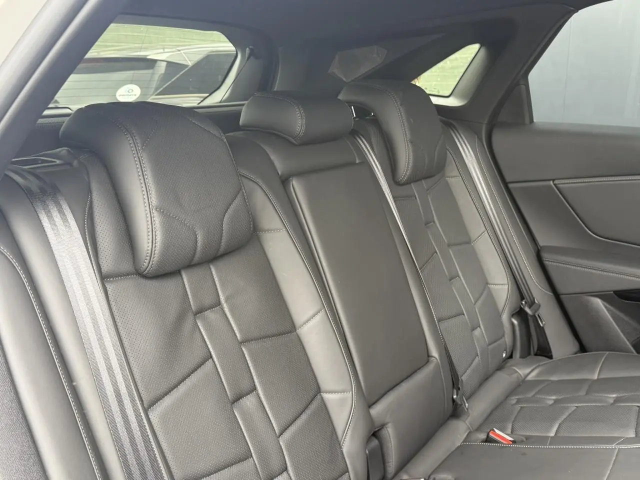 Vue intérieure sur la banquette arrière en cuir noir Basalte du DS7 2025, avec ceinture de sécurité et vitres latérales.