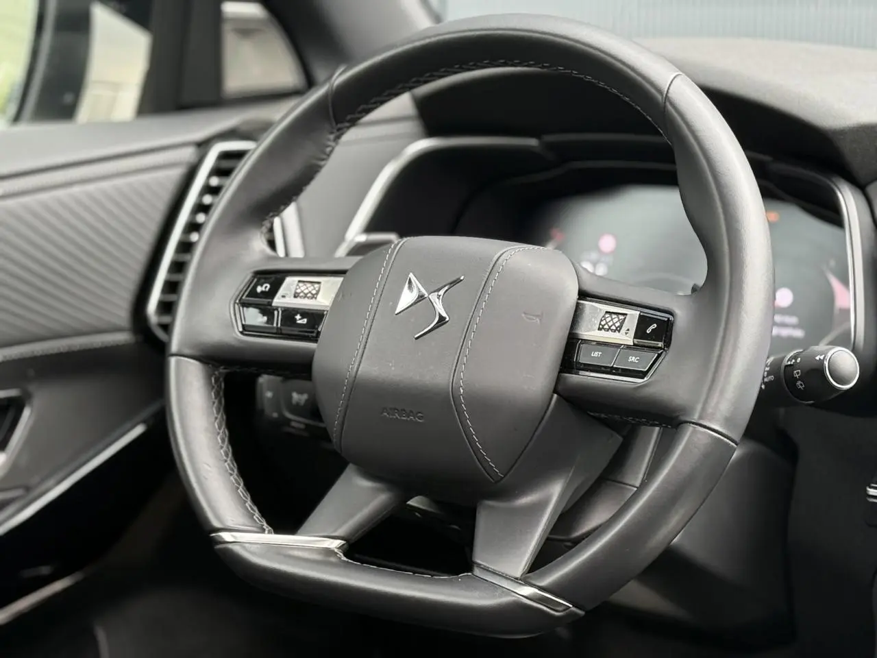 Gros plan sur le volant en cuir noir du DS7 2025, avec commandes intégrées et logo DS au centre.
