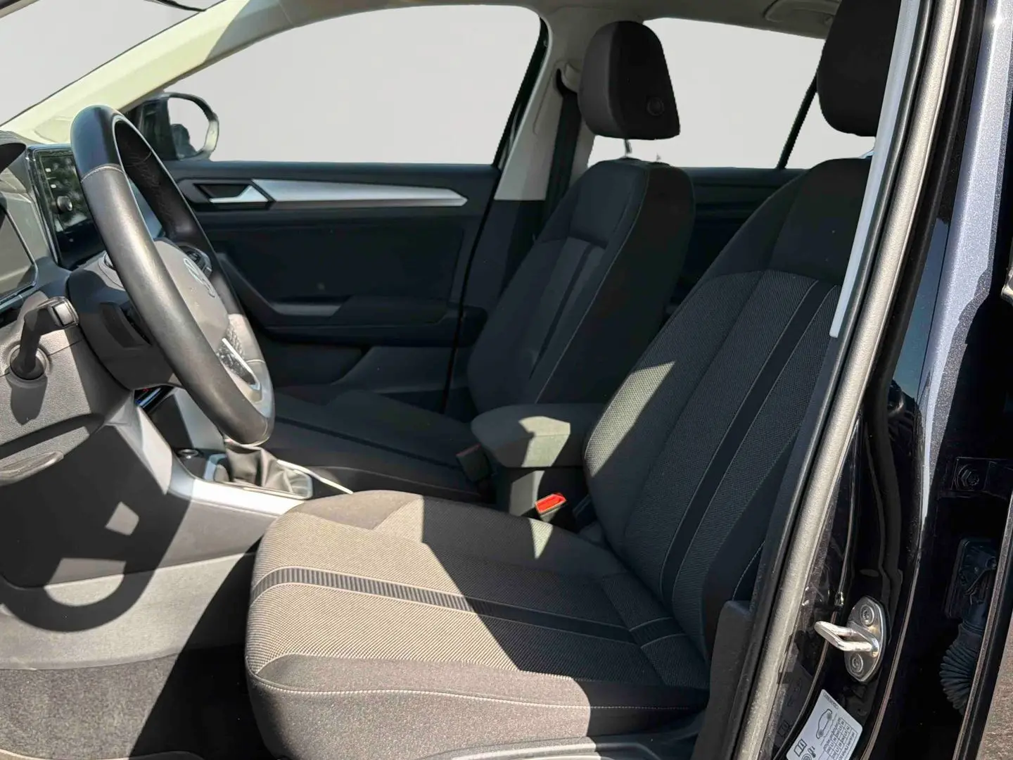 Intérieur avant droit du Volkswagen T-Roc noir 2025, sièges tissu gris et volant multifonctions visible.