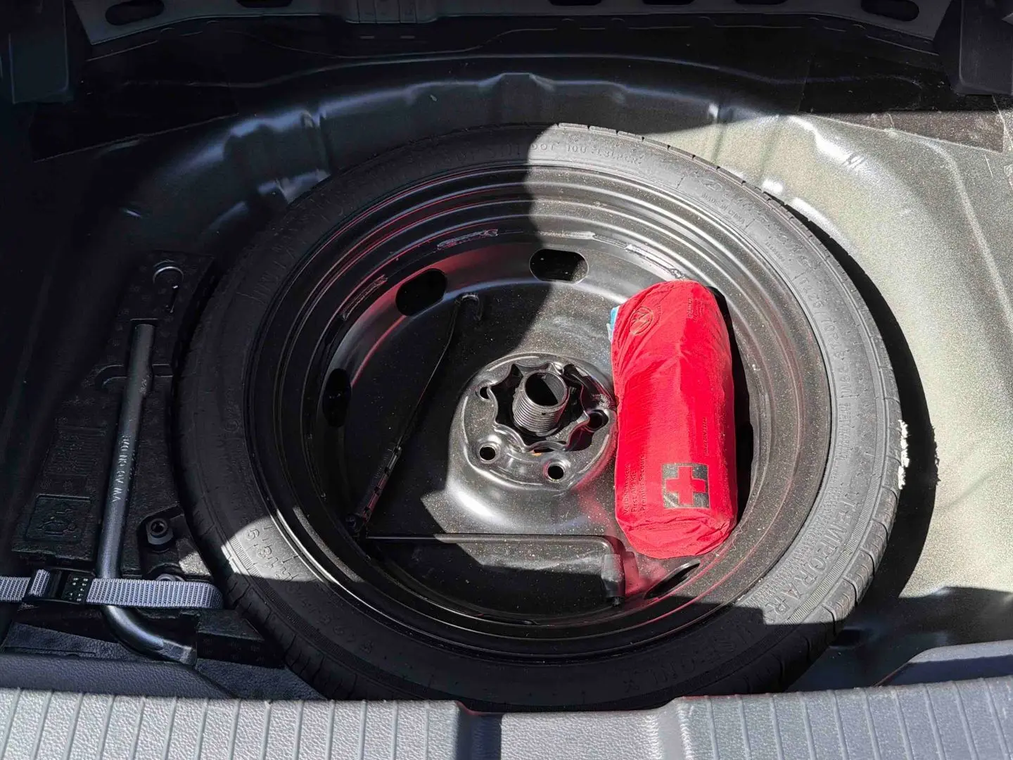 Gros plan sur la roue de secours noire du coffre d’un Volkswagen T-Roc 2025 avec trousse de secours rouge.