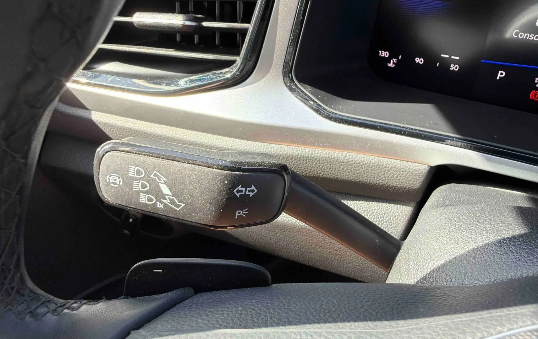Gros plan sur la commande de clignotant et feux du Volkswagen T-Roc noir, intérieur côté gauche du volant.