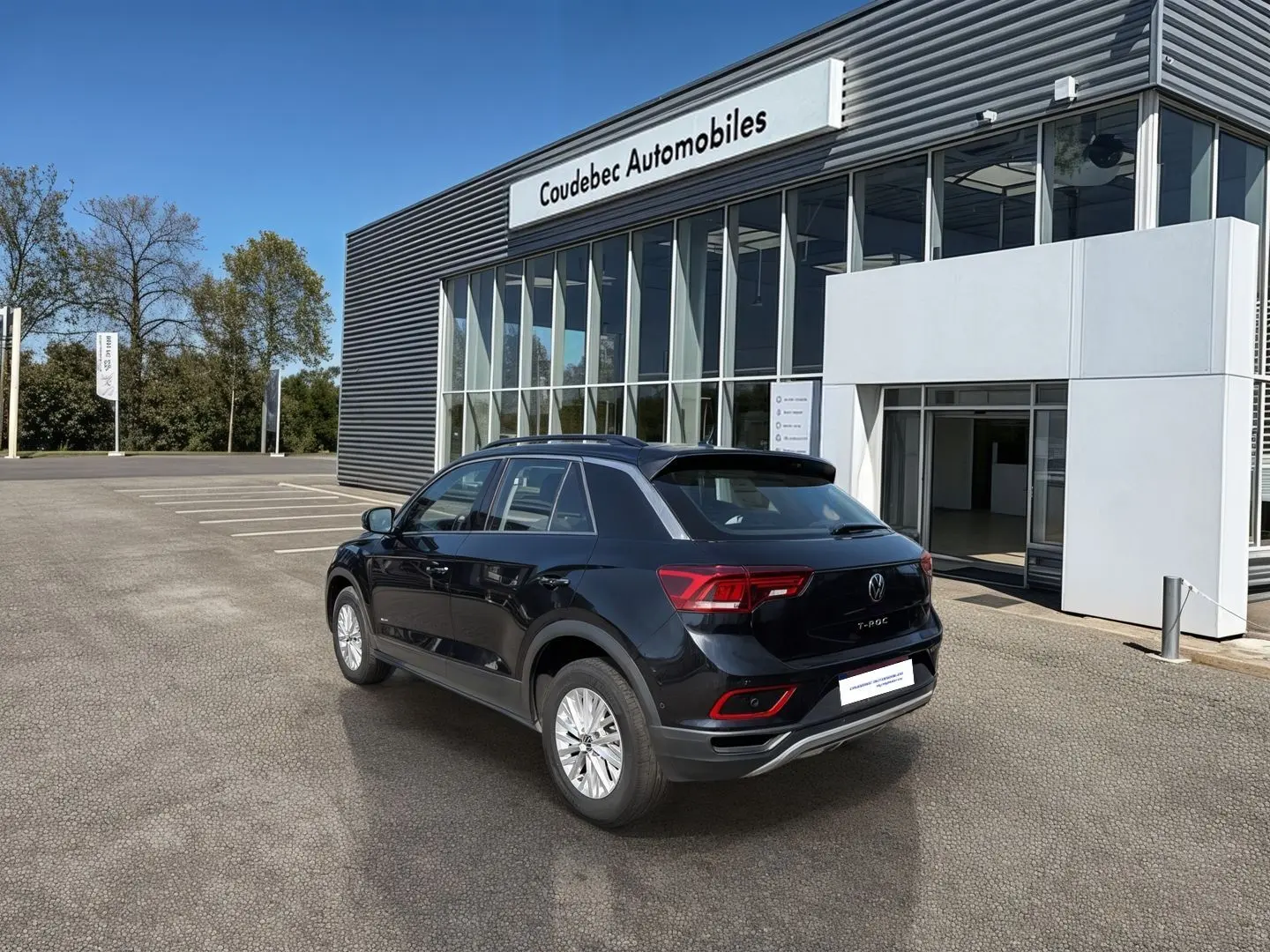 Volkswagen T-Roc noir vue 3/4 arrière droit, stationné devant un bâtiment moderne de concession automobile.