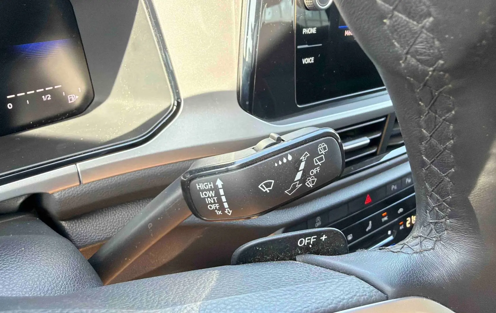 Gros plan sur le commodo d’essuie-glace et partie du volant cuir du Volkswagen T-Roc noir, tableau de bord digital en arrière-plan.