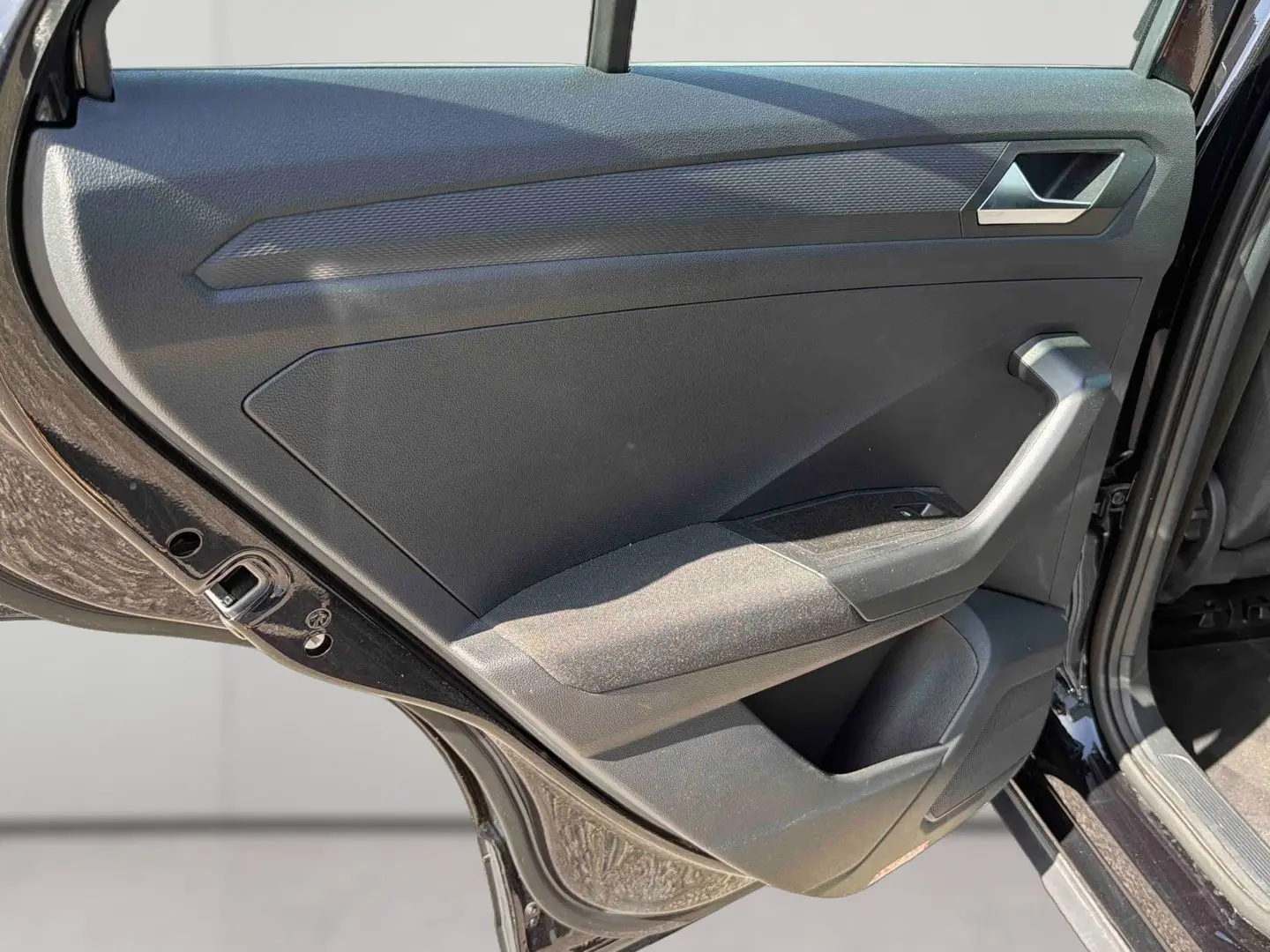 Vue intérieure de la porte arrière gauche noire du Volkswagen T-Roc 2025 avec accoudoir et commande de vitre.